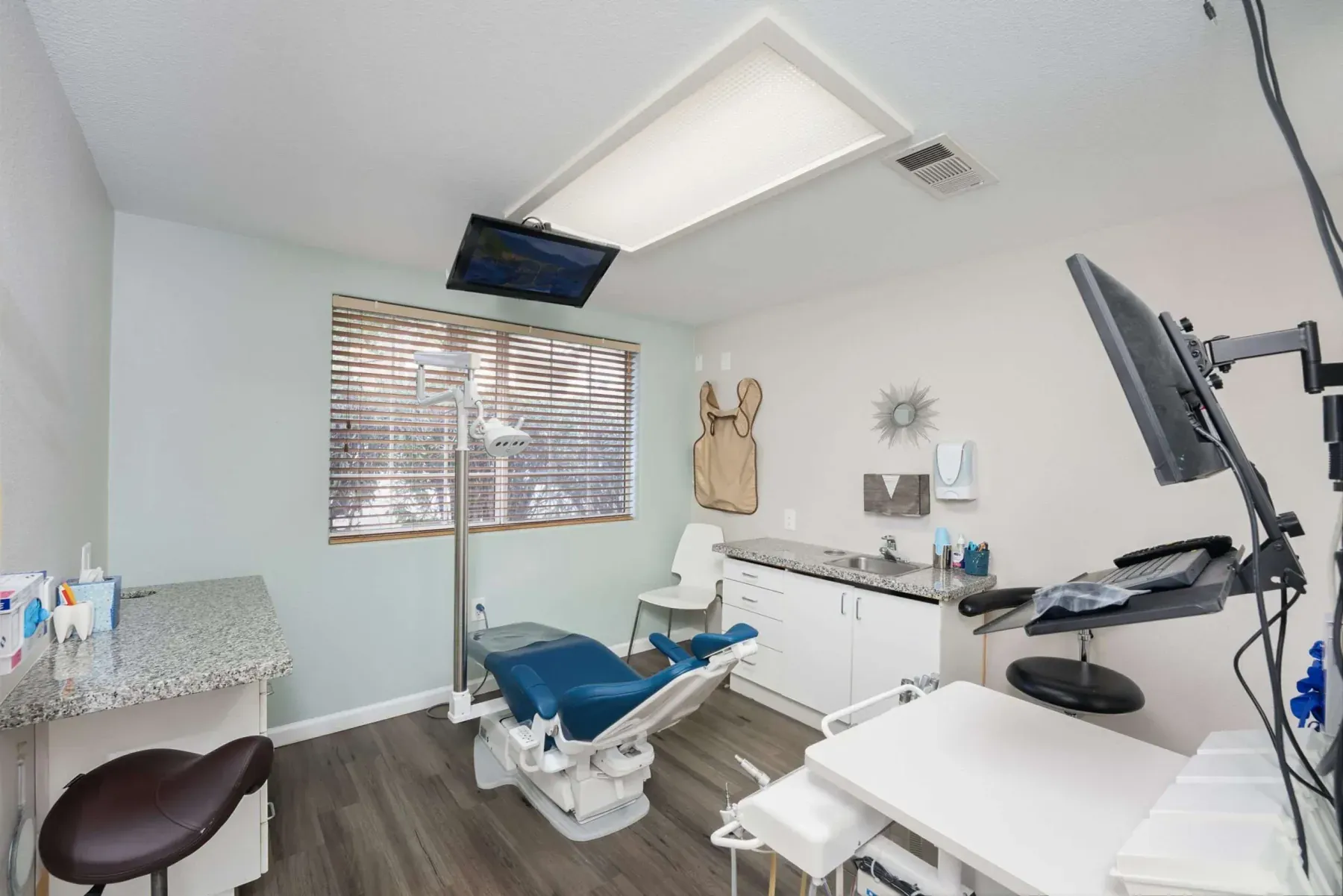 A treatment room with a blue dental chair beneath the window