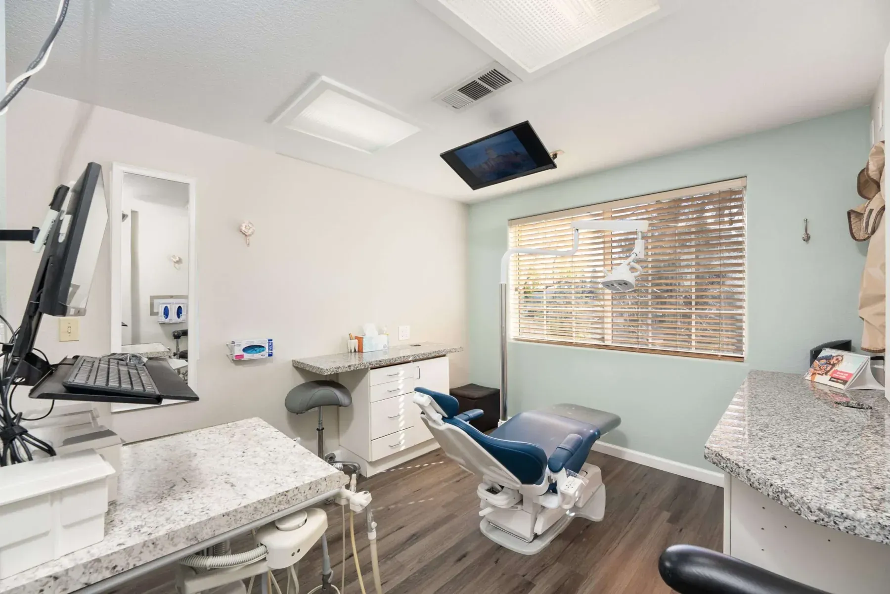 A treatment room with a window, granite counters, and a ceiling-mounted screen